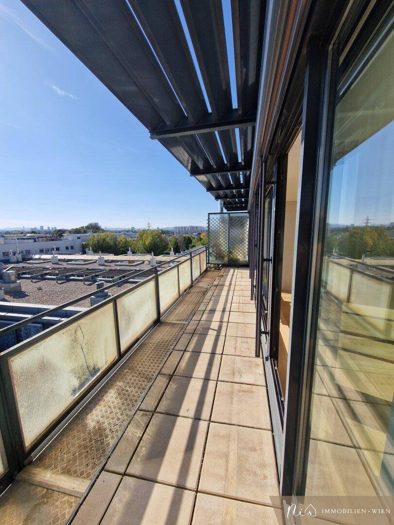 Langer Balkon mit Fliesenboden und Glasgeländer, bietet einen weiten Blick über die Stadt.
