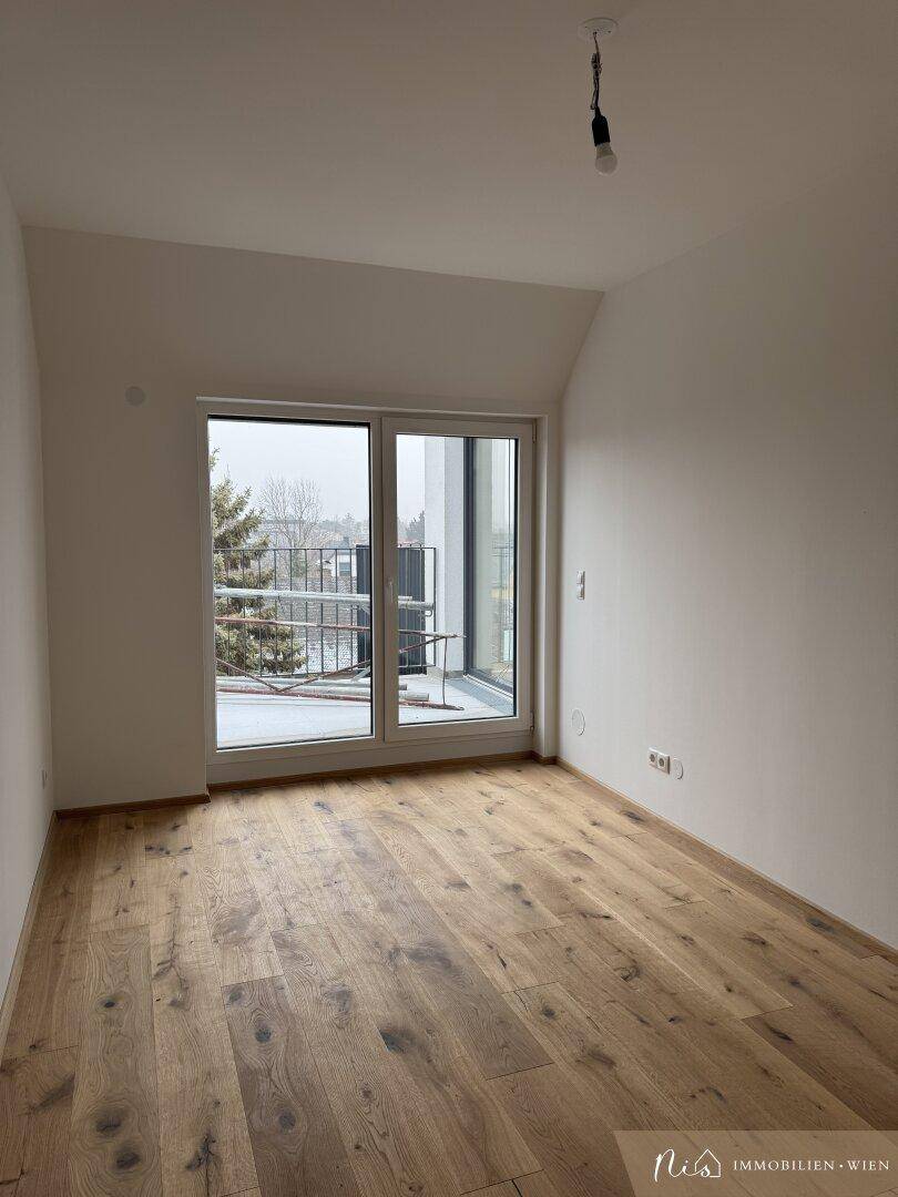Leeres Zimmer mit Holzboden und großem Fenster, das Zugang zu einem Balkon bietet.