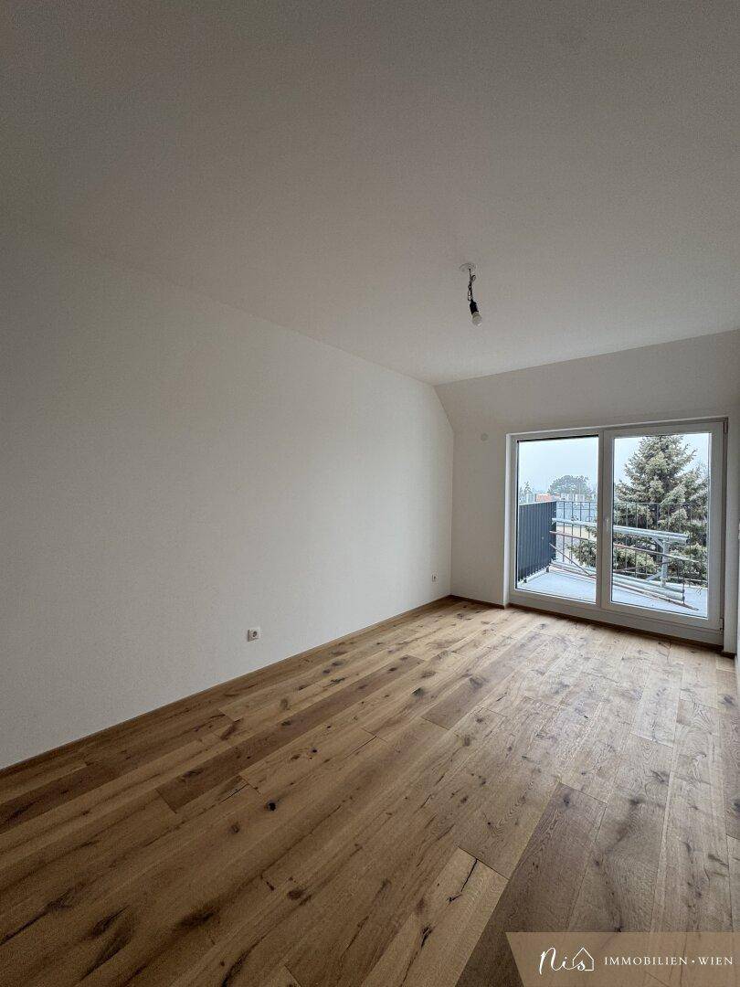 Leeres Zimmer mit Holzboden und großem Fenster, das Zugang zu einem Balkon bietet.