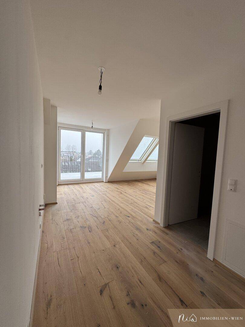 Heller, leerer Raum mit Holzboden, großen Fenstern und Zugang zu einem Balkon oder einer Terrasse.