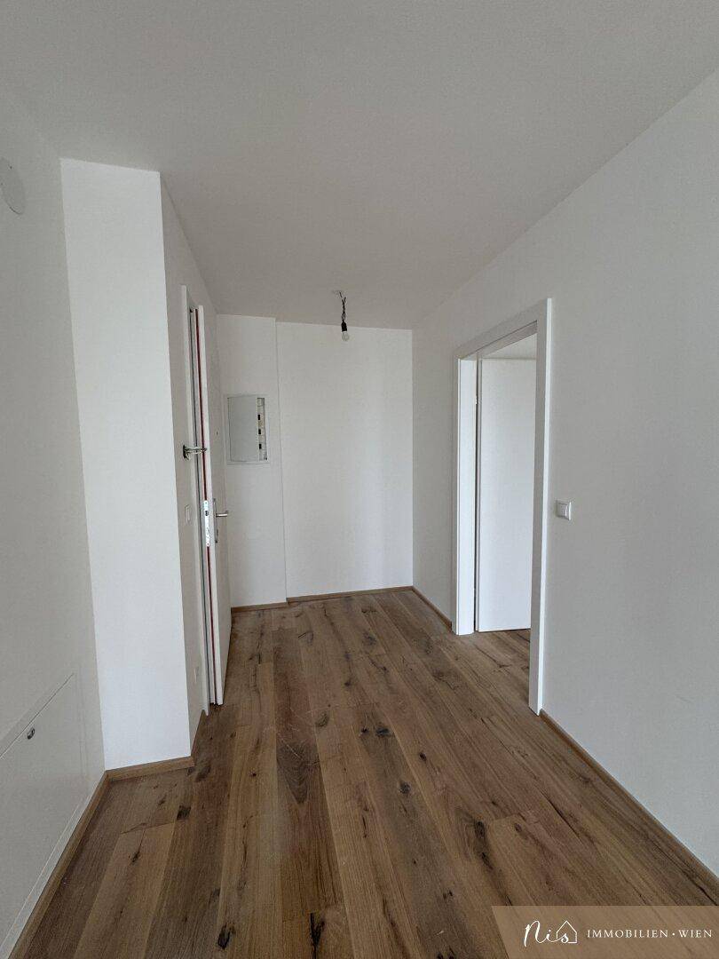 Heller Flur mit Holzboden und weißen Wänden, der zu weiteren Räumen führt.