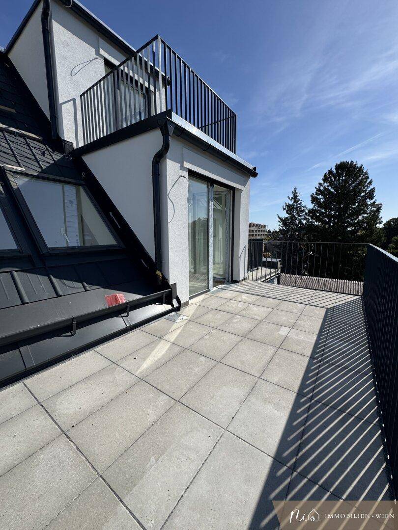 Geräumige Dachterrasse mit Fliesenboden und schwarzem Geländer unter blauem Himmel.