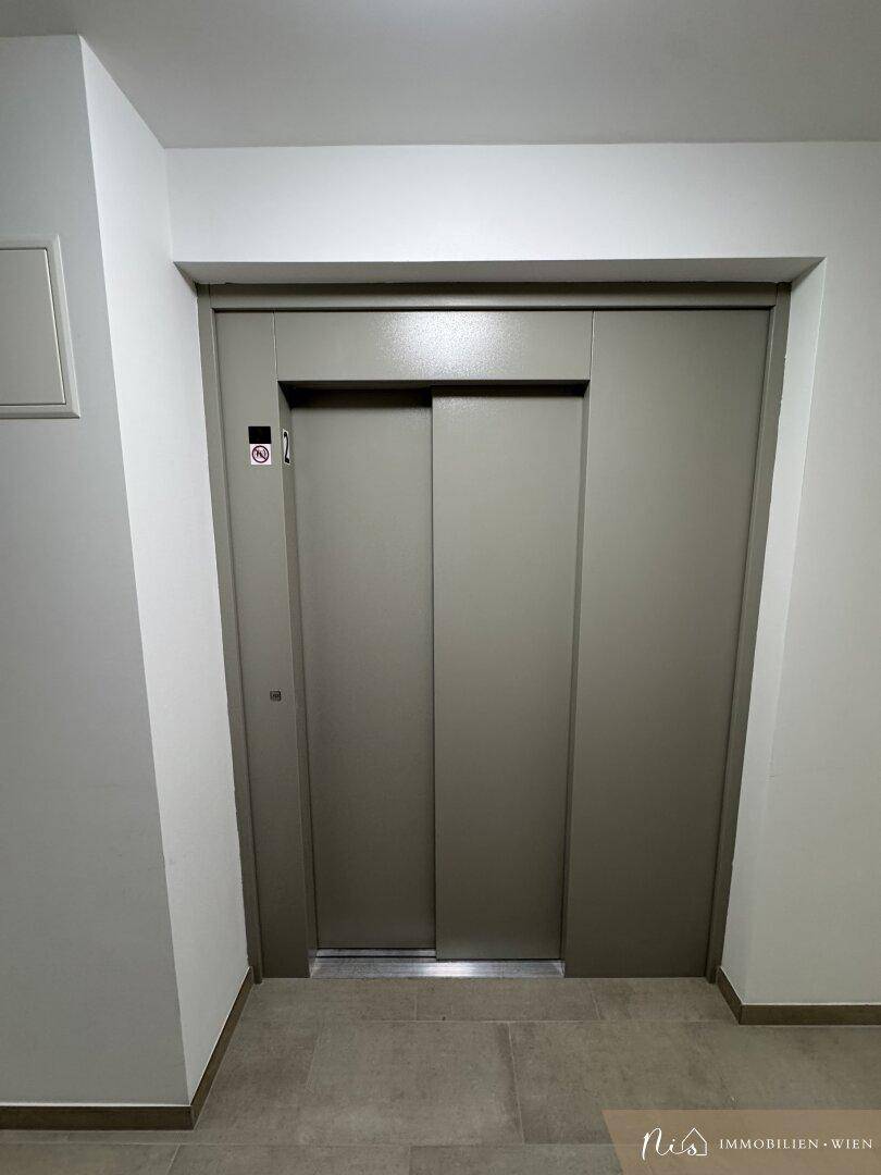 Heller Flur mit Fliesenboden und Aufzugstür in einem modernen Gebäude.