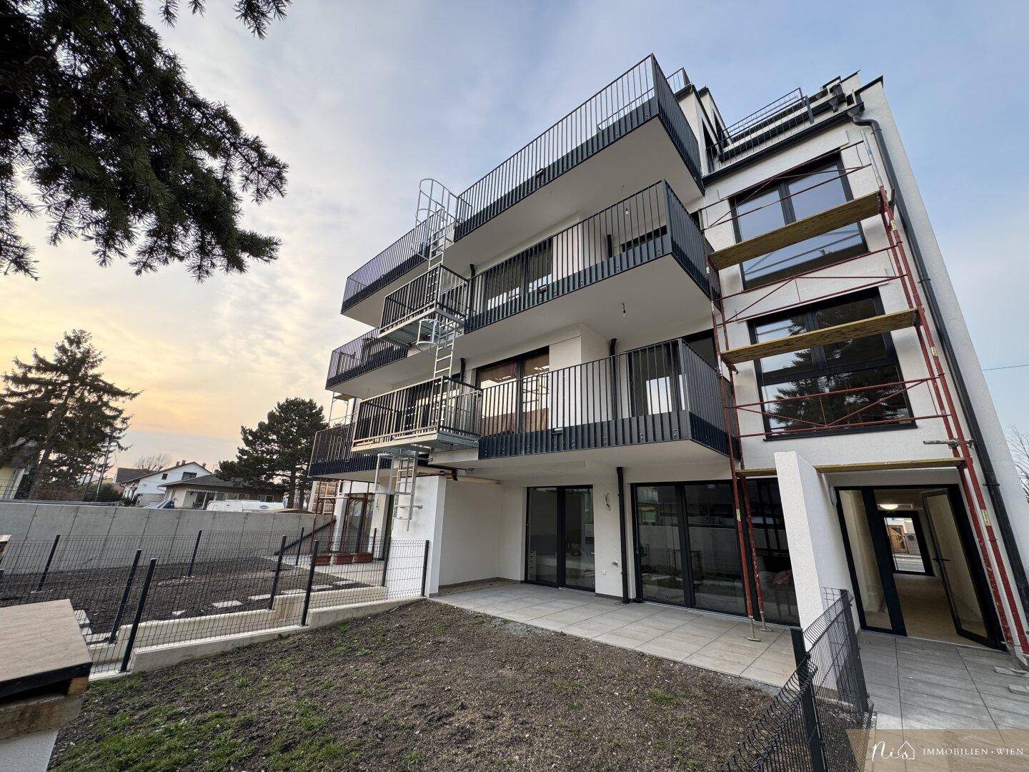 Moderne Wohnanlage im Neubau mit mehreren Balkonen und Außentreppe bei Sonnenuntergang.