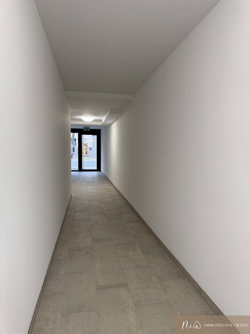 Langer, heller Flur mit Fliesenboden und Ausgang zu einem Außenbereich.