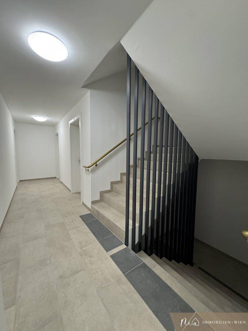 Modernes Treppenhaus mit Fliesenboden und schwarzem Geländer in einem Neubau.