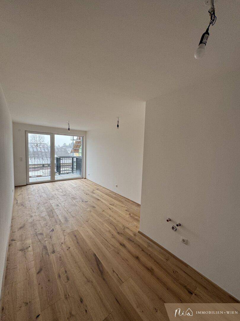 Heller, unmöblierter Wohnbereich mit Holzboden und Zugang zum Balkon.