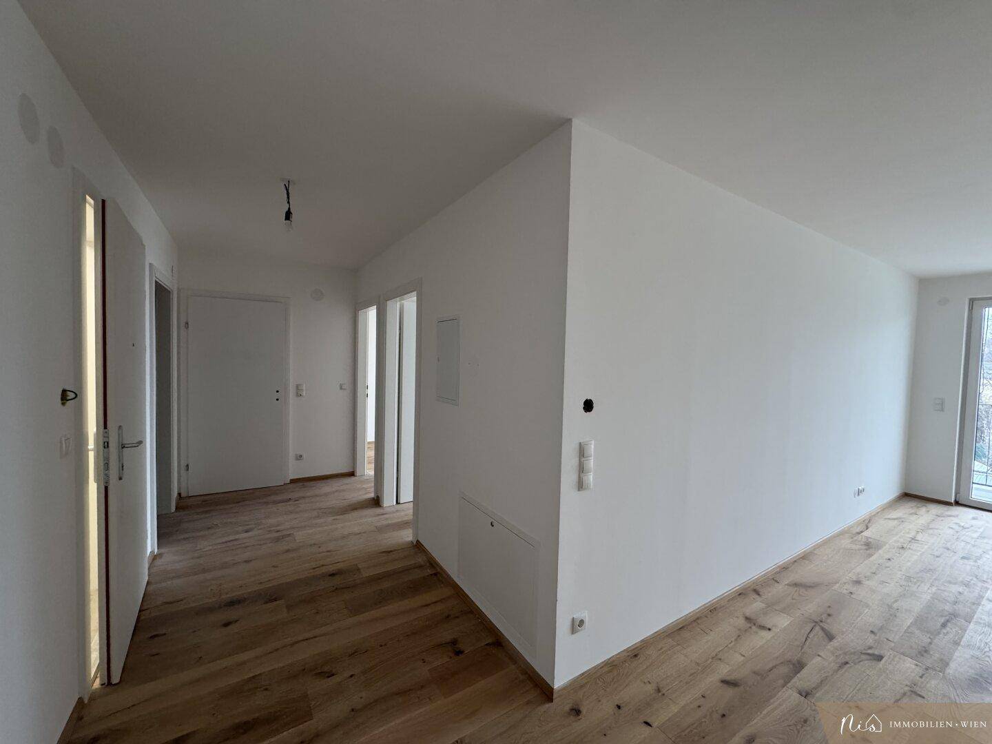 Eingangsbereich mit Holzboden und weißen Wänden, führt zu weiteren Räumen.