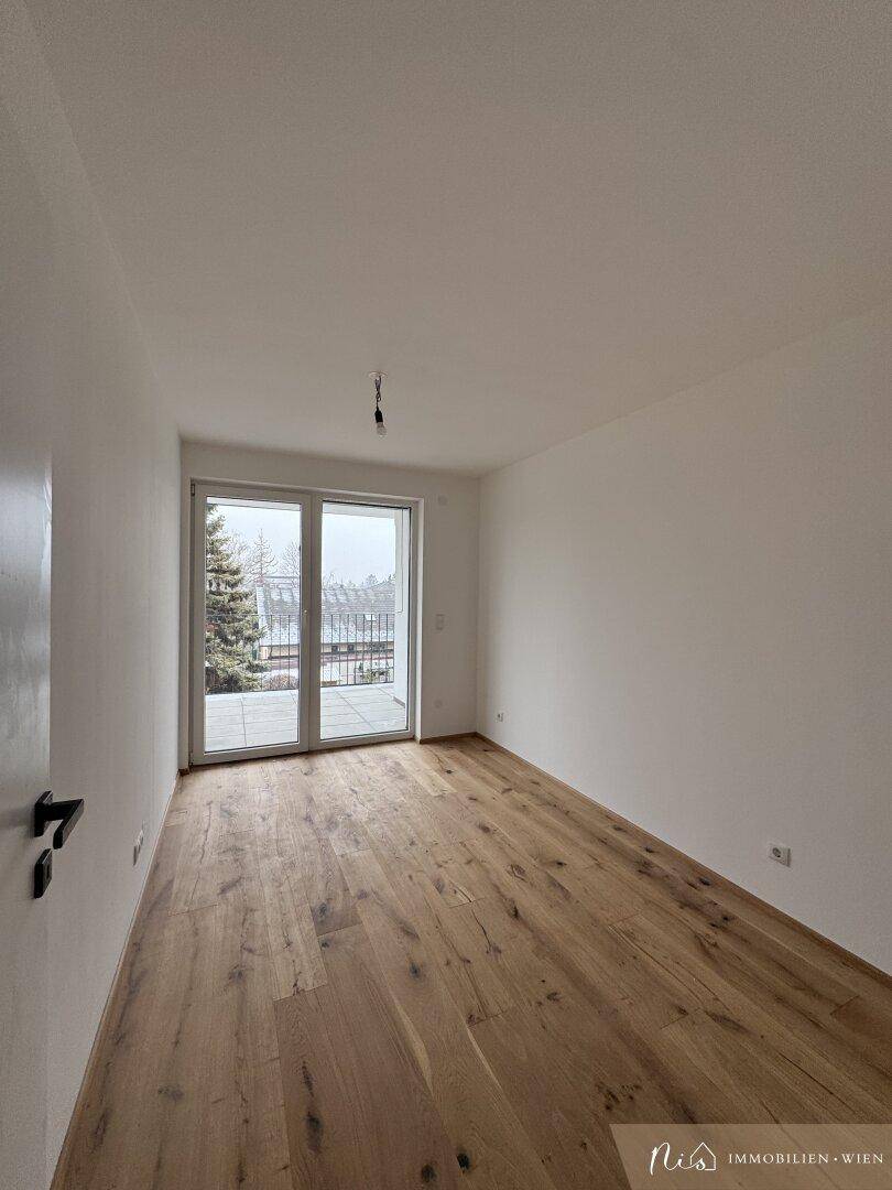 Unmöbliertes Zimmer mit Holzboden und Zugang zu einem kleinen Balkon.