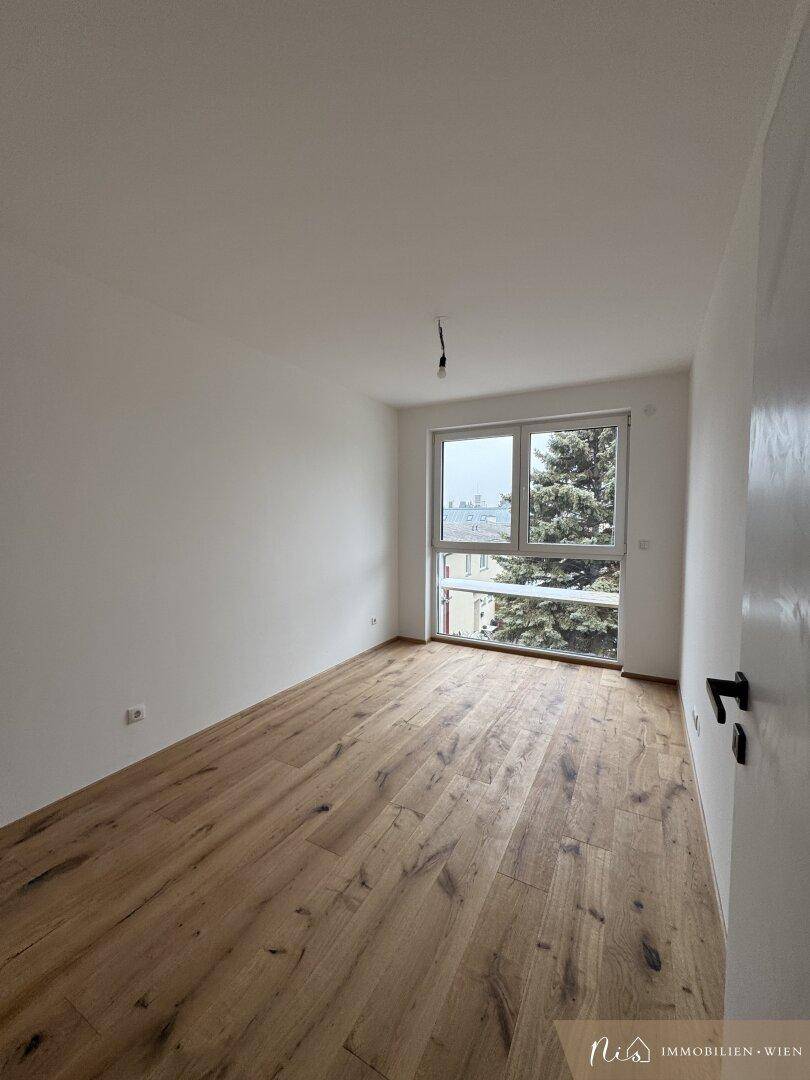 Helles Schlafzimmer mit Holzboden und großem Fenster mit Blick ins Grüne.
