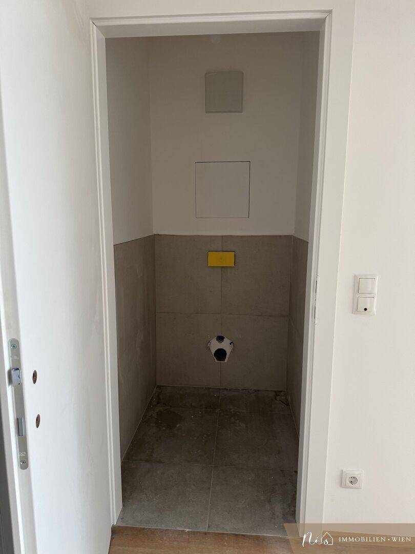 Separate Gästetoilette im Bau mit Fliesenboden und Wandanschluss.
