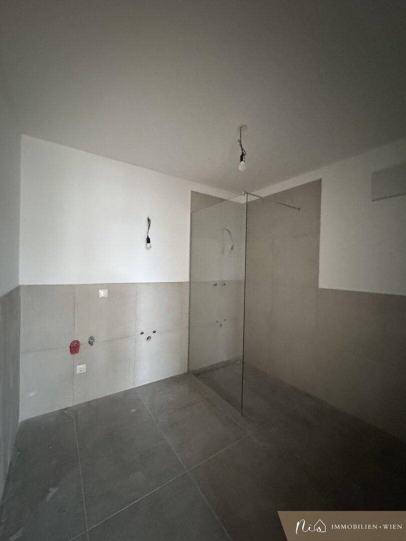 Badezimmer im Bau mit Fliesenboden und vorbereiteter Duschkabine.