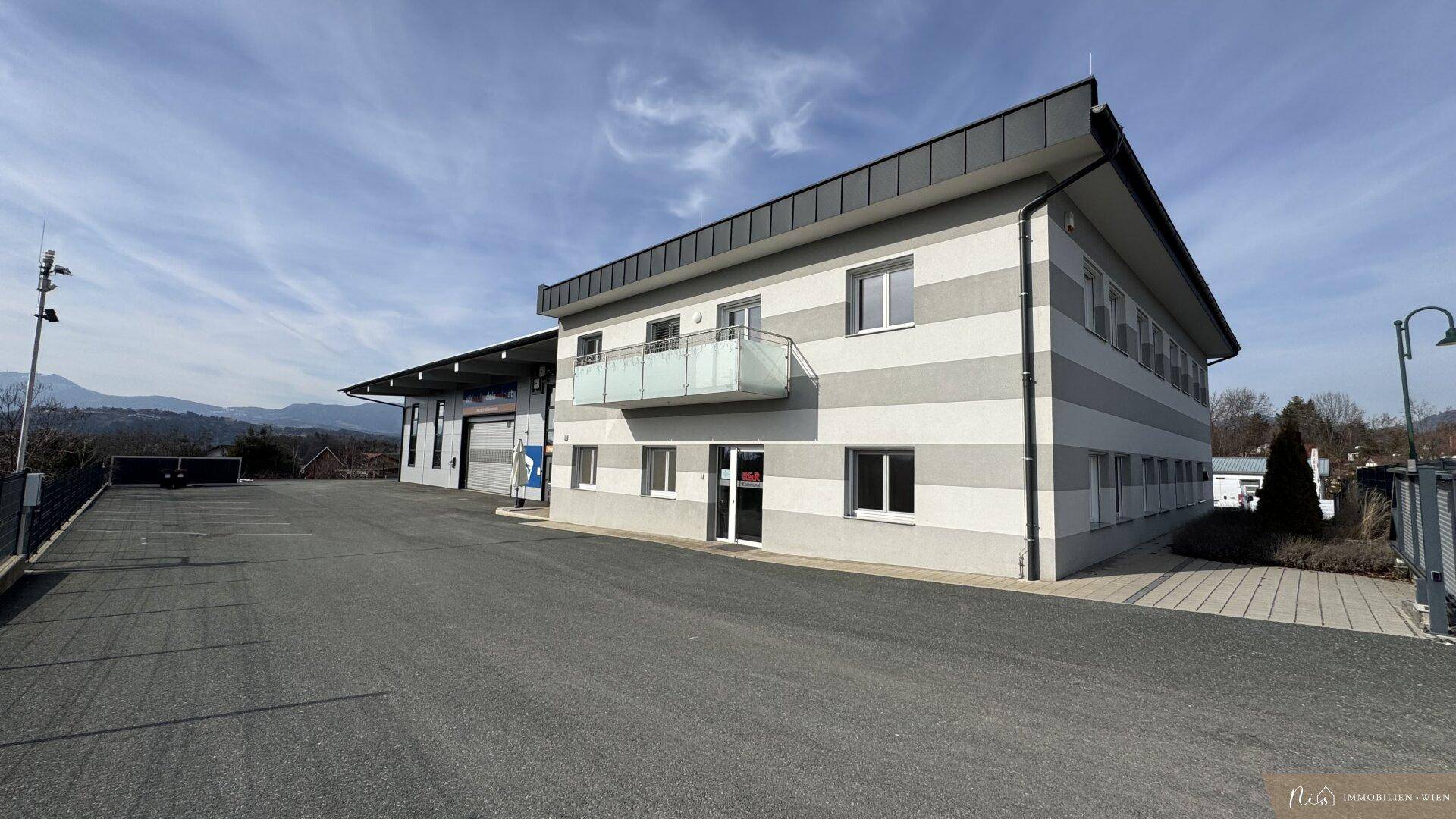 Gesamtansicht des modernen Geschäftsgebäudes mit Parkplatz und umliegender Landschaft im Hintergrund.