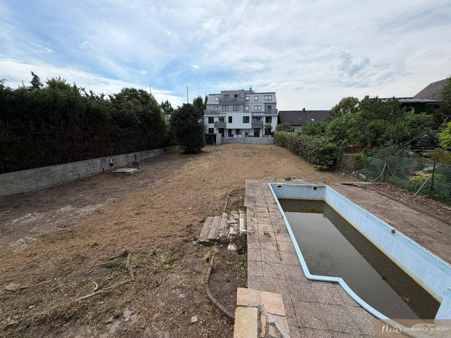 Großer Gartenbereich mit einem ungenutzten Pool und Blick auf ein Mehrfamilienhaus im Hintergrund.