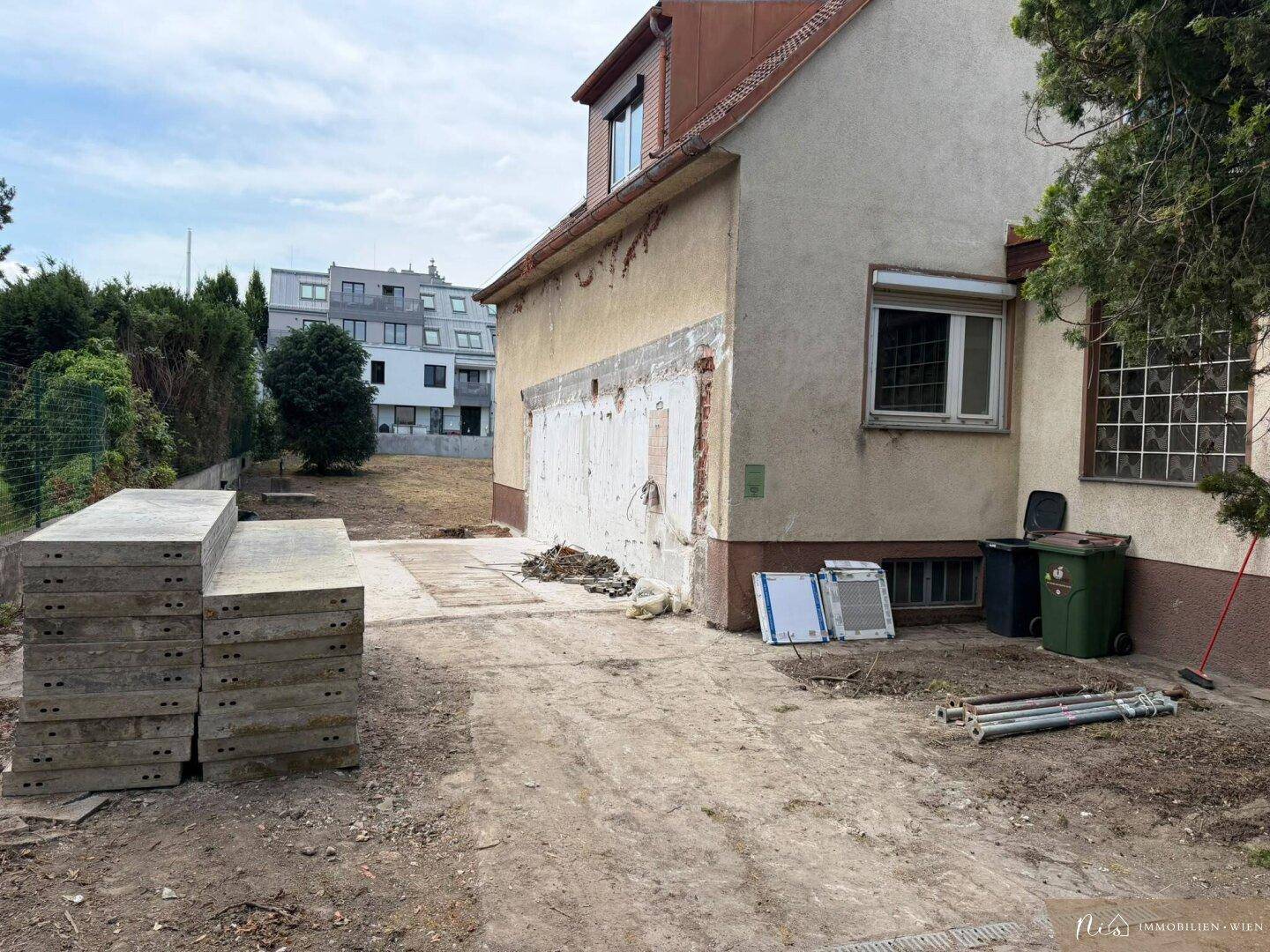 Seitenansicht des Hauses mit gestapelten Betonplatten und Bauschutt im Vordergrund.
