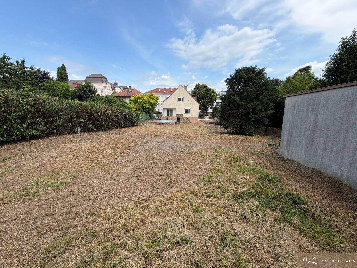 Weitläufiger Gartenbereich mit trockenem Gras und einem Einfamilienhaus in der Ferne.