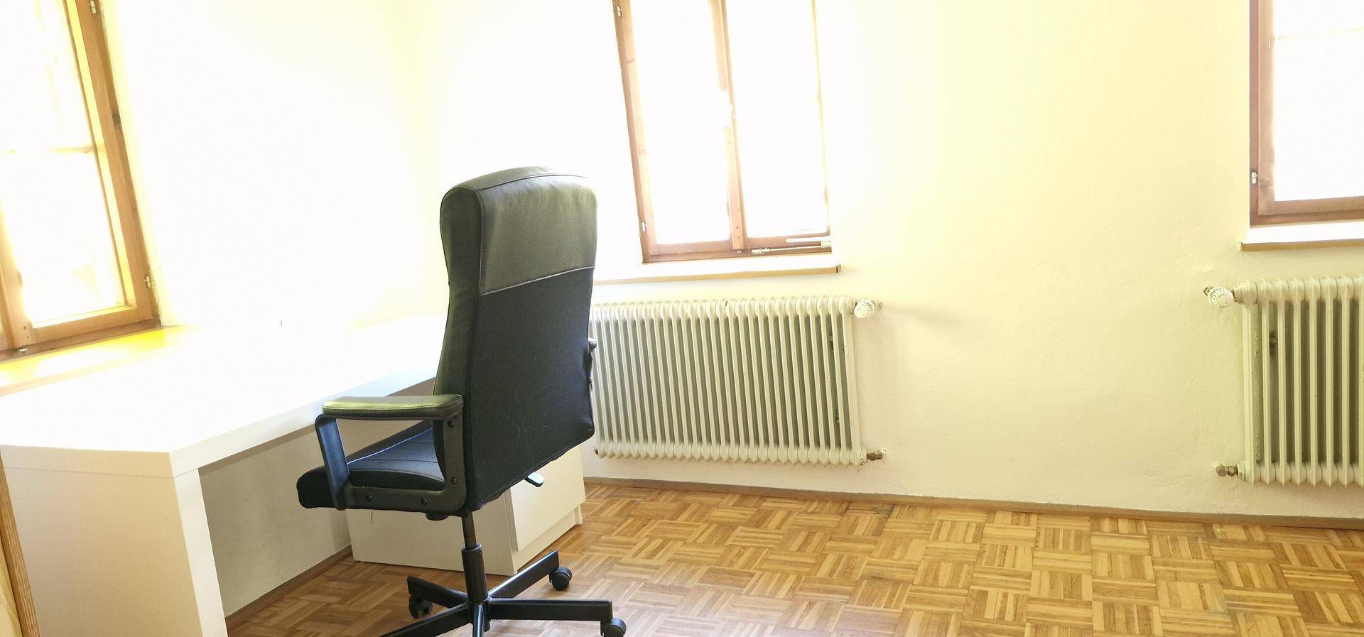 Helles Arbeitszimmer mit Schreibtisch, Bürostuhl und Parkettboden.