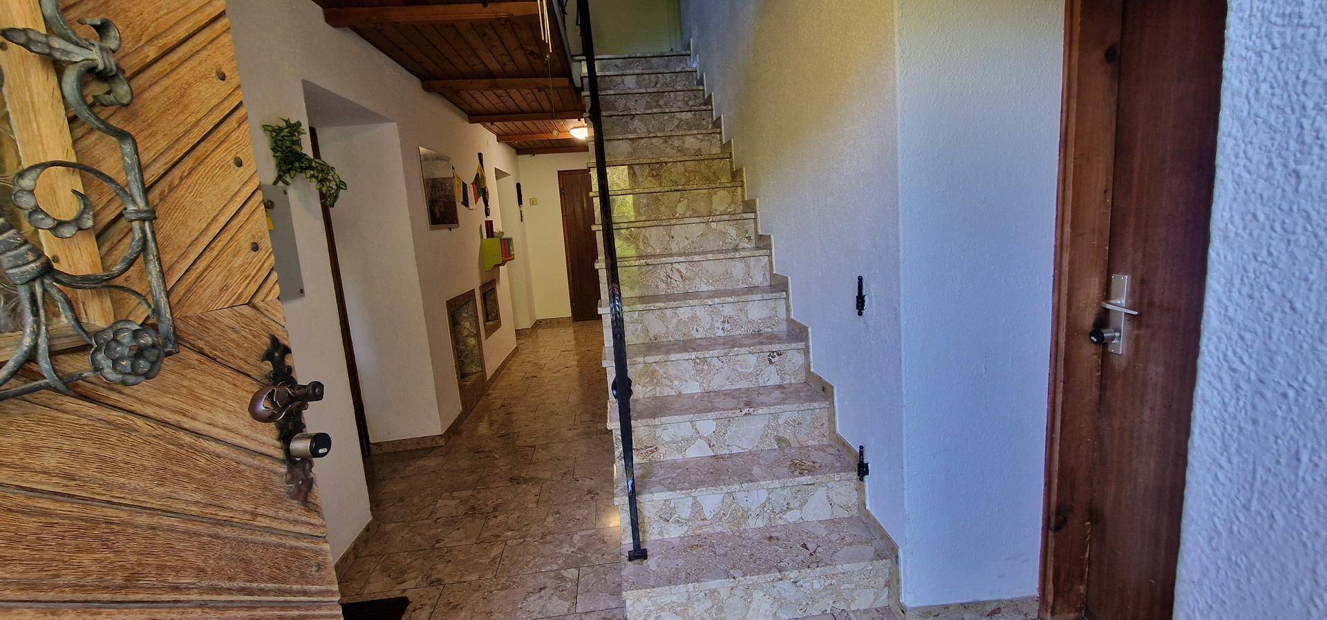 Eingangsbereich mit Treppe, Fliesenboden und Holztür mit schmiedeeisernen Details.