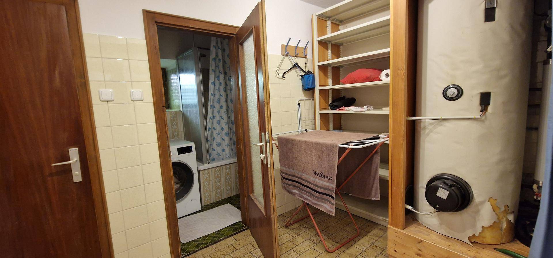 Hauswirtschaftsraum mit Waschmaschine, Warmwasserboiler und Regalen für Lagerung.