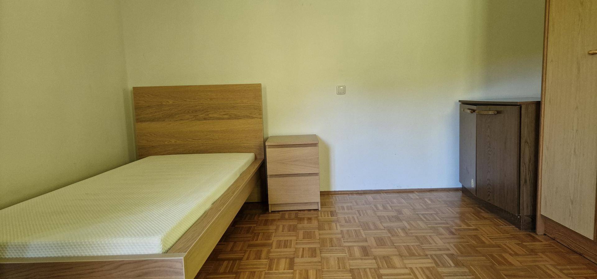 Schlafzimmer mit Einzelbett, Nachttisch und Parkettboden.