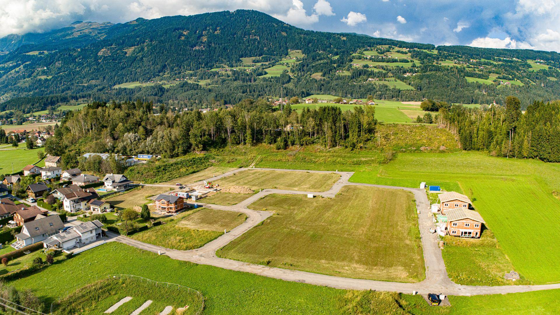 Weitläufige Luftaufnahme eines Baugebietes in grüner Landschaft mit Bergblick.