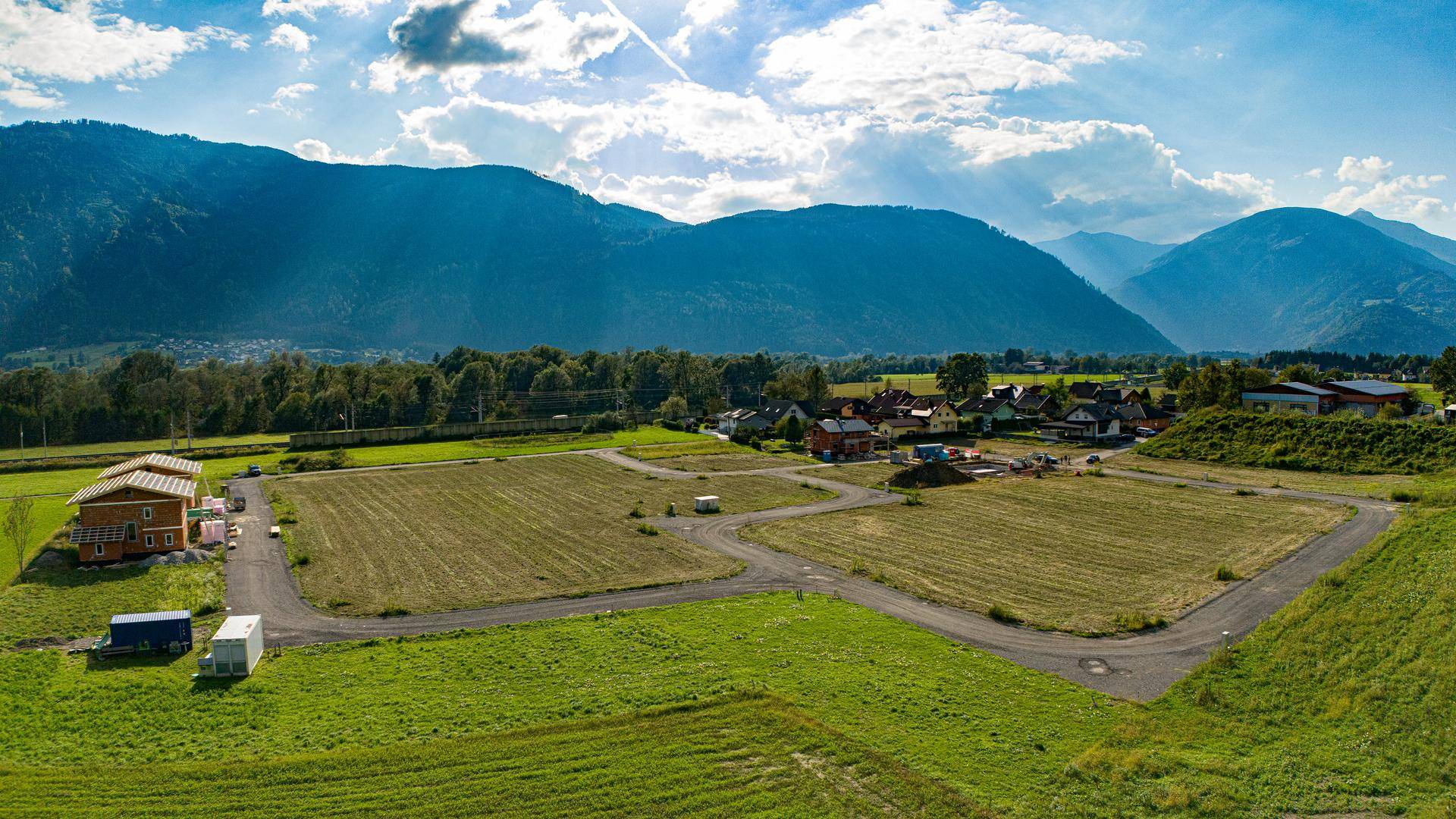 Sonnige Luftaufnahme eines ländlichen Baugebiets mit beeindruckendem Blick auf die umliegenden Berge.