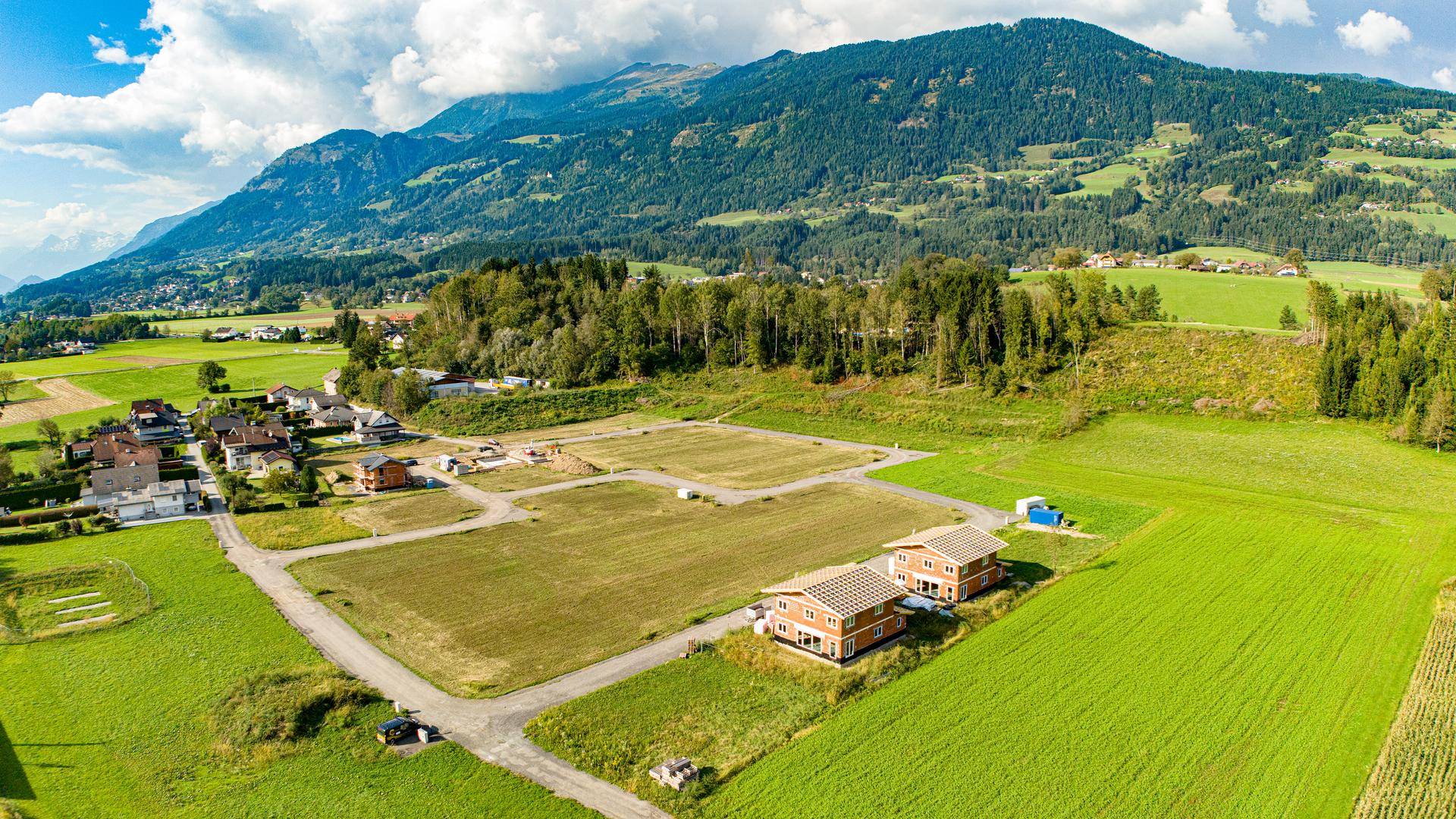 Luftaufnahme eines Wohngebiets mit Neubauten und freien Baugrundstücken vor einer Bergkulisse.