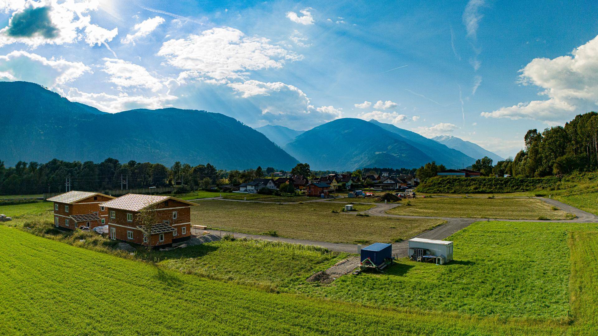 Panoramablick auf zwei neue Holzhäuser in einer ländlichen Umgebung mit Bergblick.