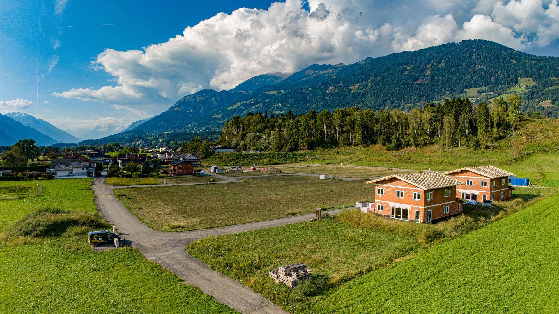 Panoramablick auf zwei neue Ziegelhäuser in ländlicher Umgebung mit grünen Feldern.