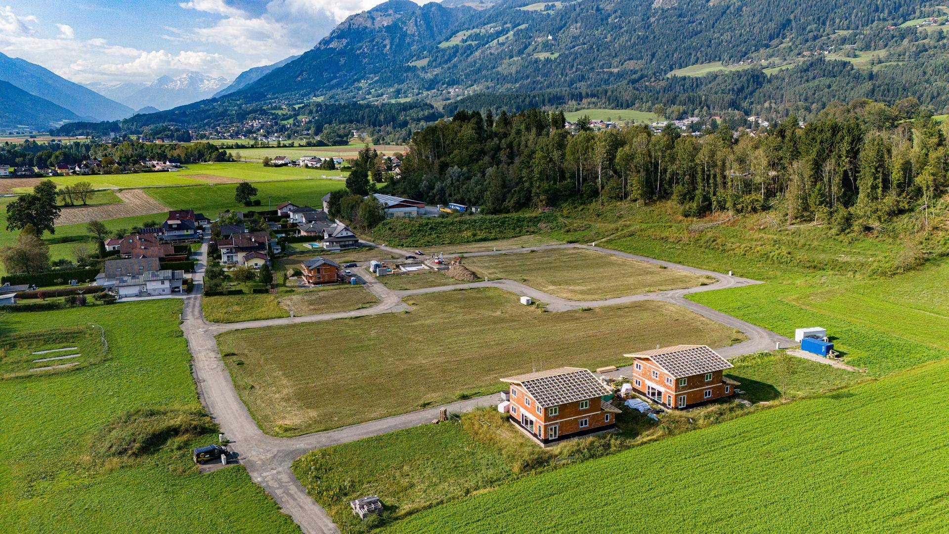 Luftaufnahme eines Neubaugebietes mit im Bau befindlichen Holzhäusern und freien Grundstücken in ländlicher Umgebung.