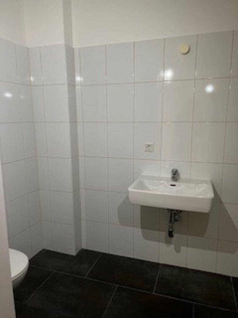 Sauberer WC-Bereich mit Waschbecken, weißen Wandfliesen und dunklem Fliesenboden.