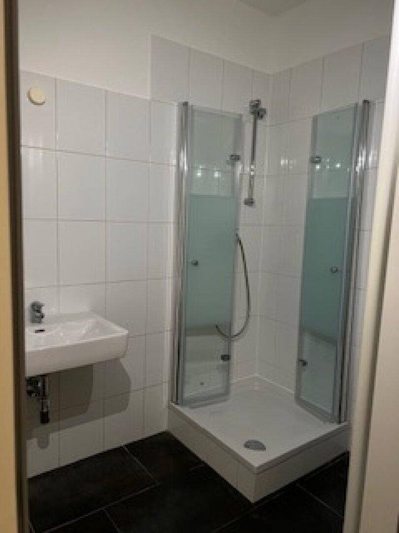 Modernes Badezimmer mit weiß gefliesten Wänden, dunklem Boden und einer Duschkabine mit Glasabtrennung.