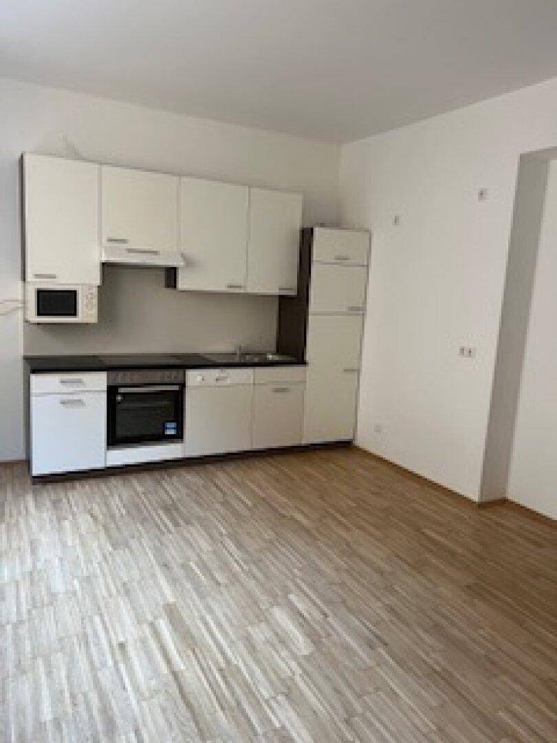 Funktionale Küchenzeile mit integrierten Geräten und hellem Holzparkett in einem unmöblierten Raum.