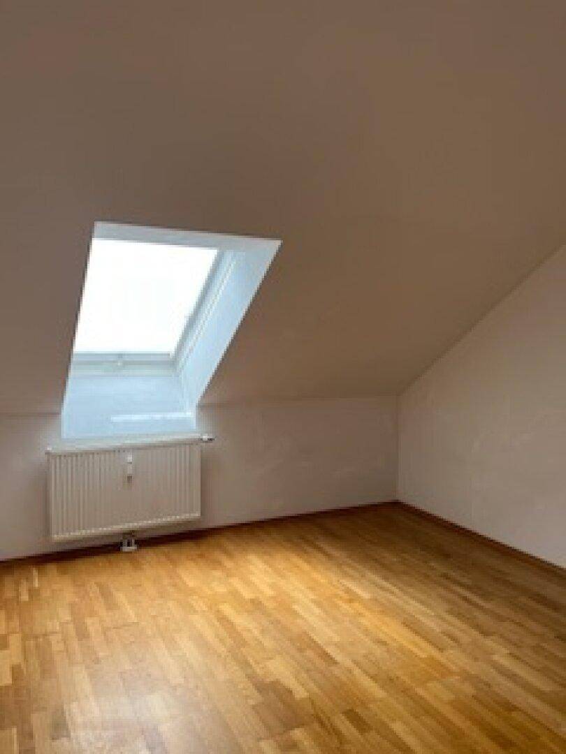 Lichtdurchfluteter Dachgeschossraum mit Parkettboden und einem großen Dachfenster für viel Tageslicht.