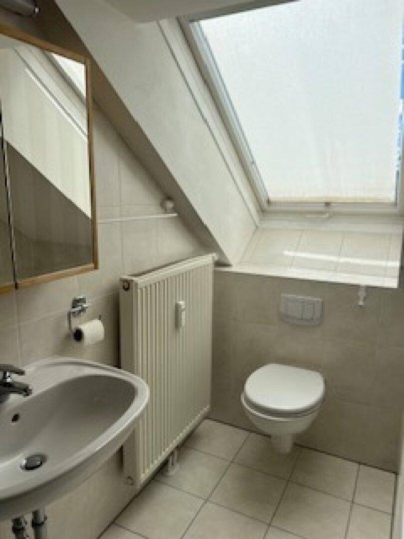 Badezimmer im Dachgeschoss mit WC, Waschbecken und einem Dachfenster für natürliche Belüftung.