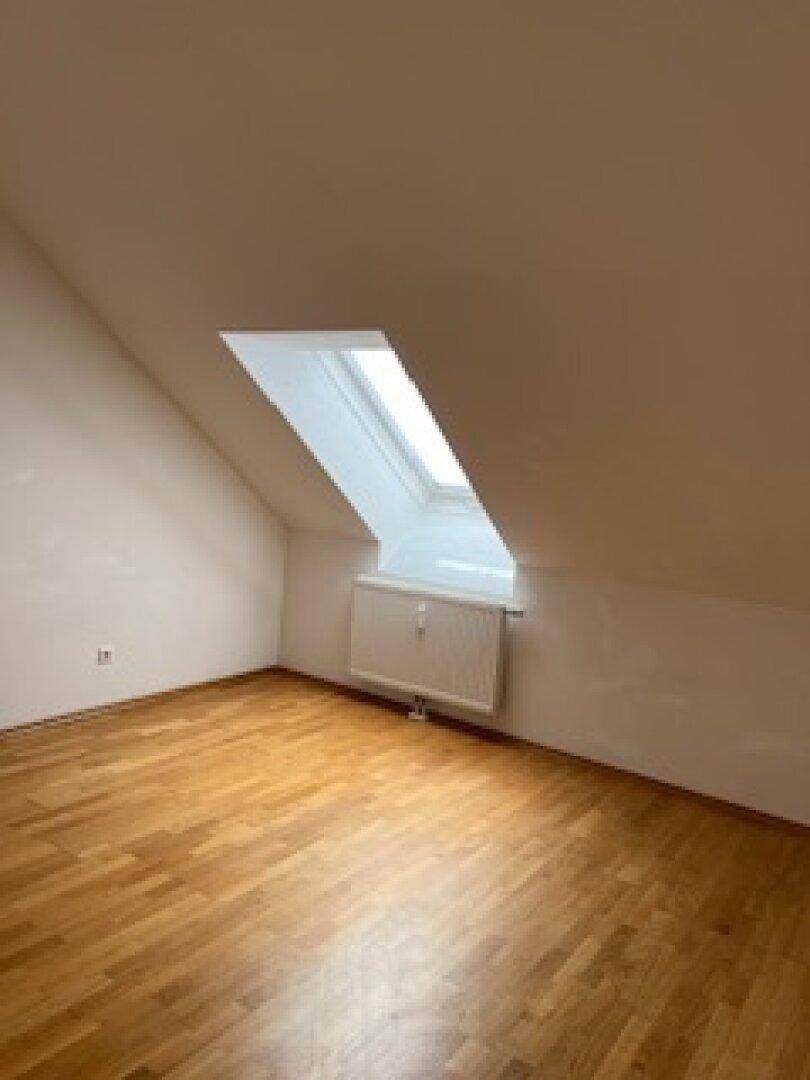 Heller Raum im Dachgeschoss mit Parkettboden und einem schrägen Dachfenster.