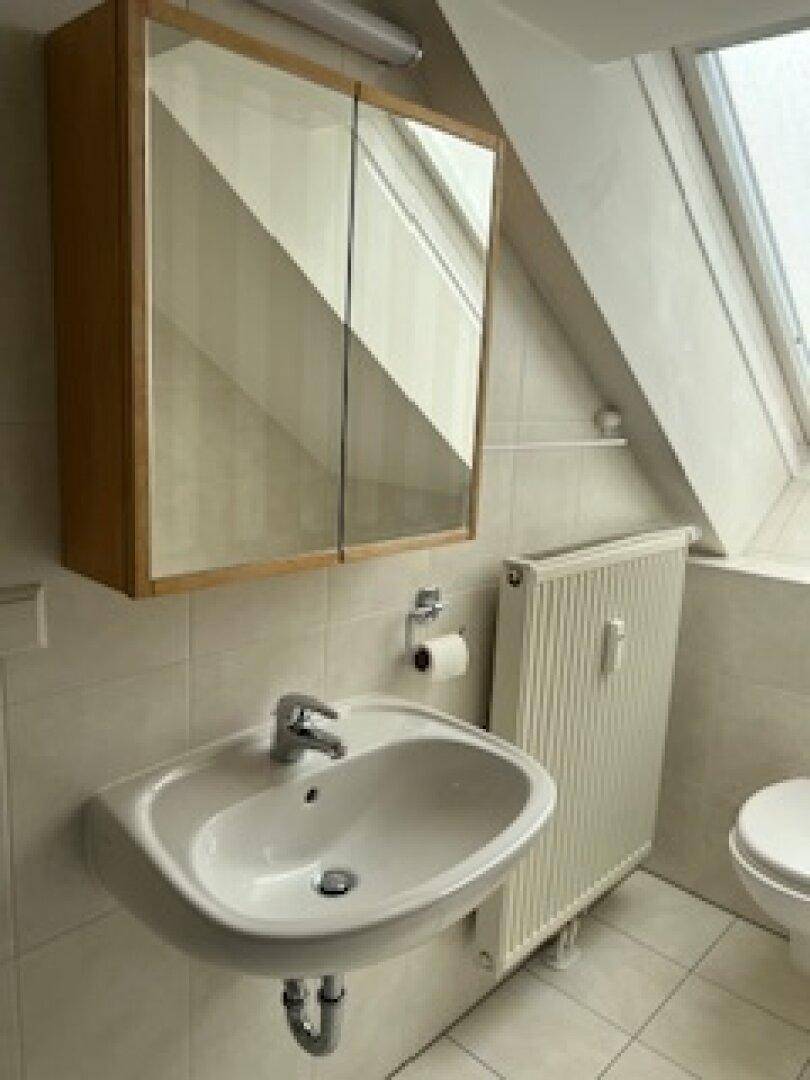 Helles Badezimmer im Dachgeschoss mit Waschbecken, Spiegelschrank und Fliesenboden.