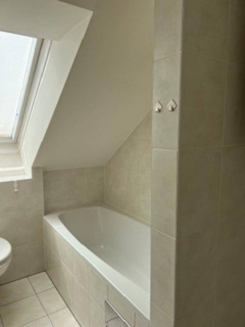Eingebaute Badewanne im Dachgeschoss-Badezimmer mit Fliesen und schräger Decke.