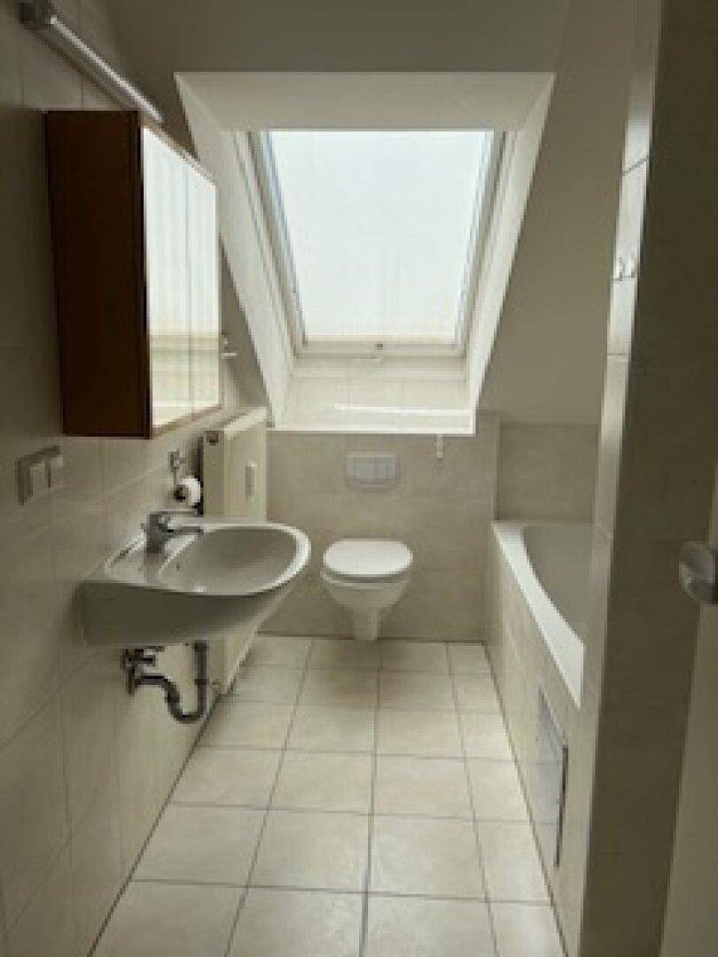 Komplettes Badezimmer im Dachgeschoss mit Badewanne, WC, Waschbecken und Dachfenster.