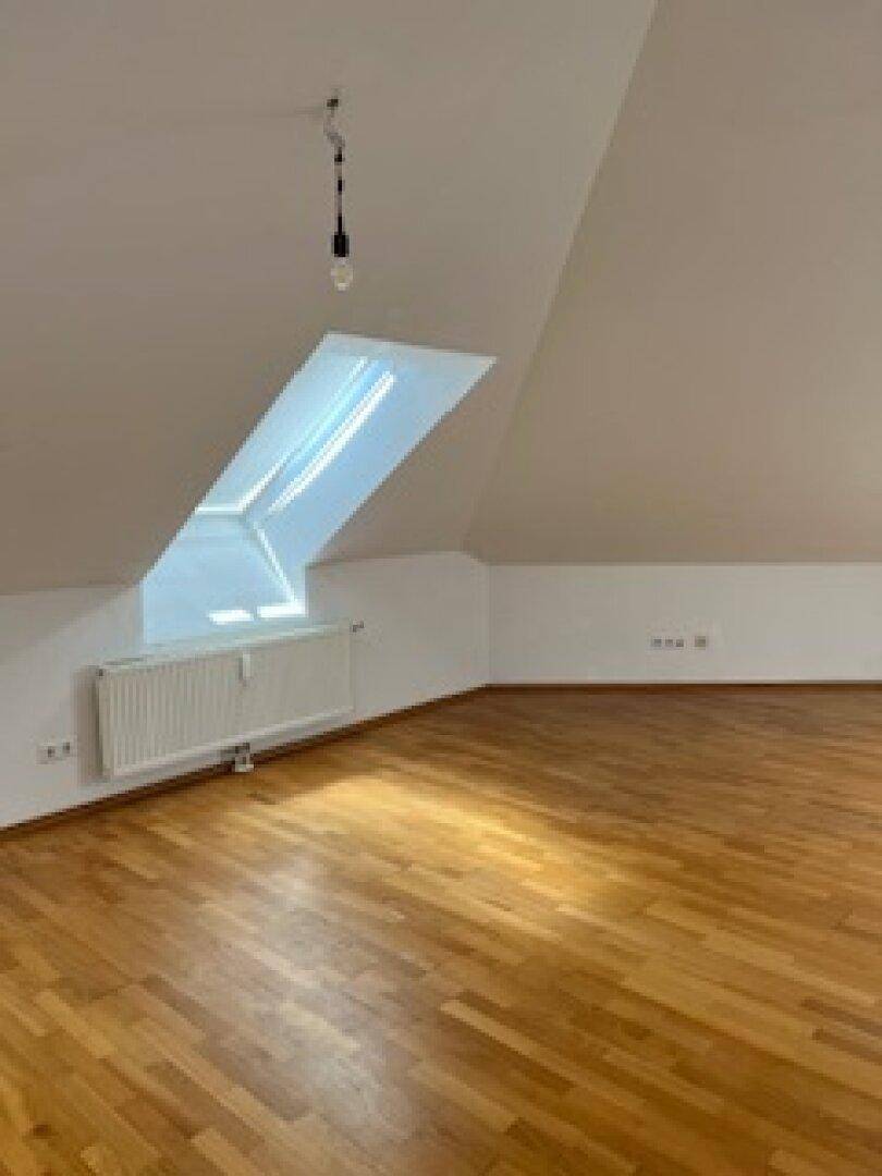 Heller Wohnraum im Dachgeschoss mit Parkettboden, Dachfenster und Heizkörper unter der Schräge.