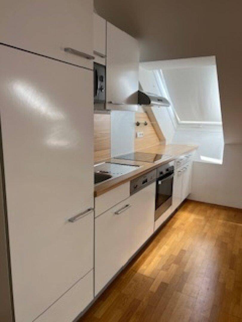 Moderne Küchenzeile im Dachgeschoss mit weißen Fronten, Holz-Arbeitsplatte und integrierten Geräten.