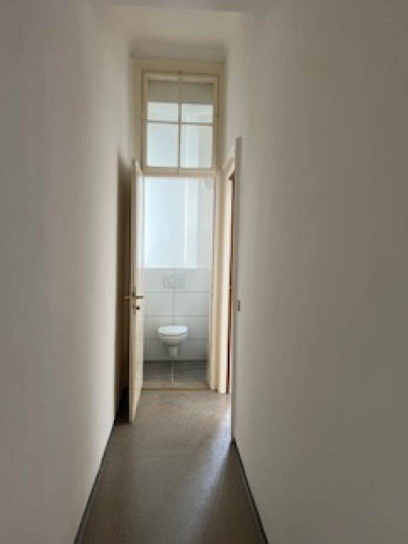 Flur mit Blick auf ein separates WC mit Fenster und weißer Toilette.