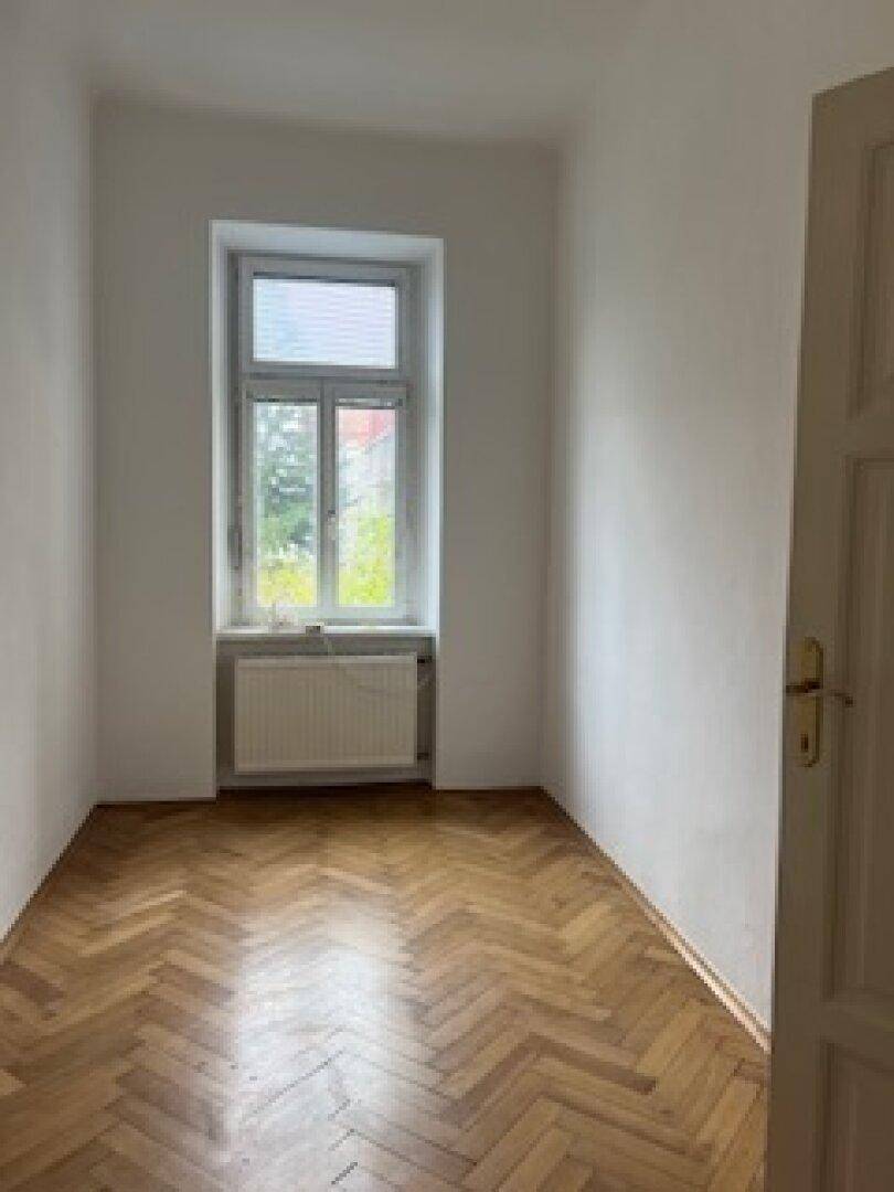 Helles Schlafzimmer mit Fischgrätparkett und großem Fenster.