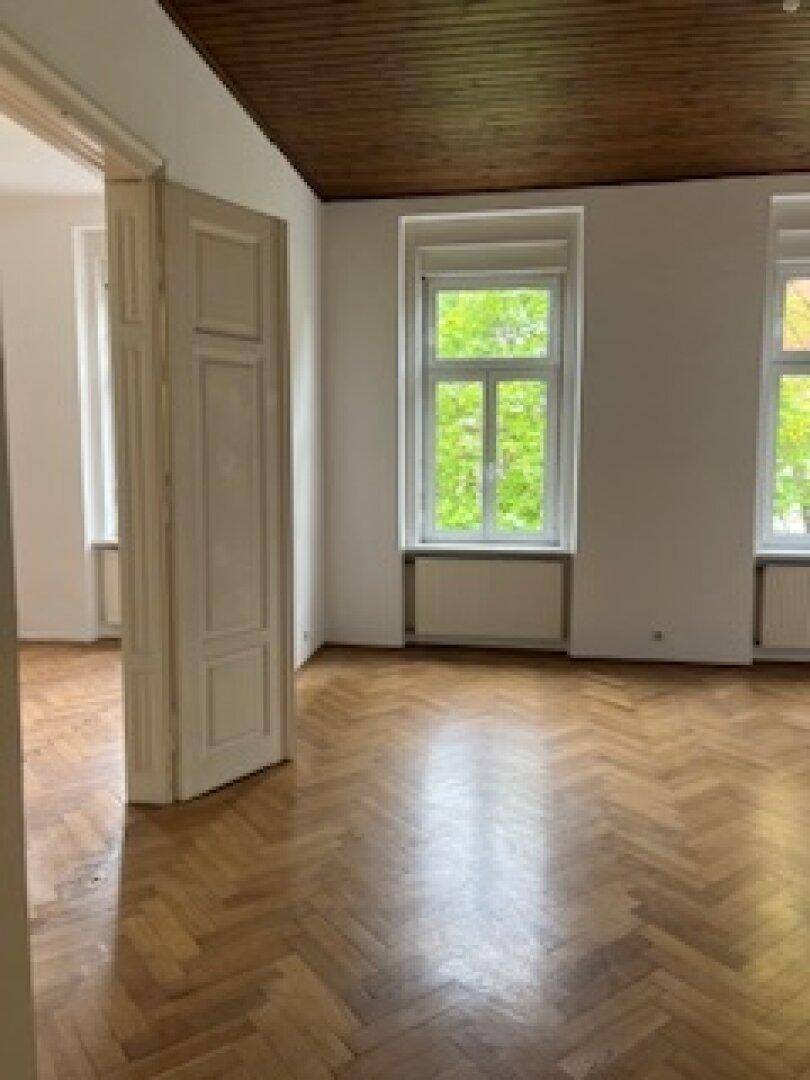 Geräumiges Wohnzimmer mit Fischgrätparkett, Holzbalkendecke und großen Fenstern.