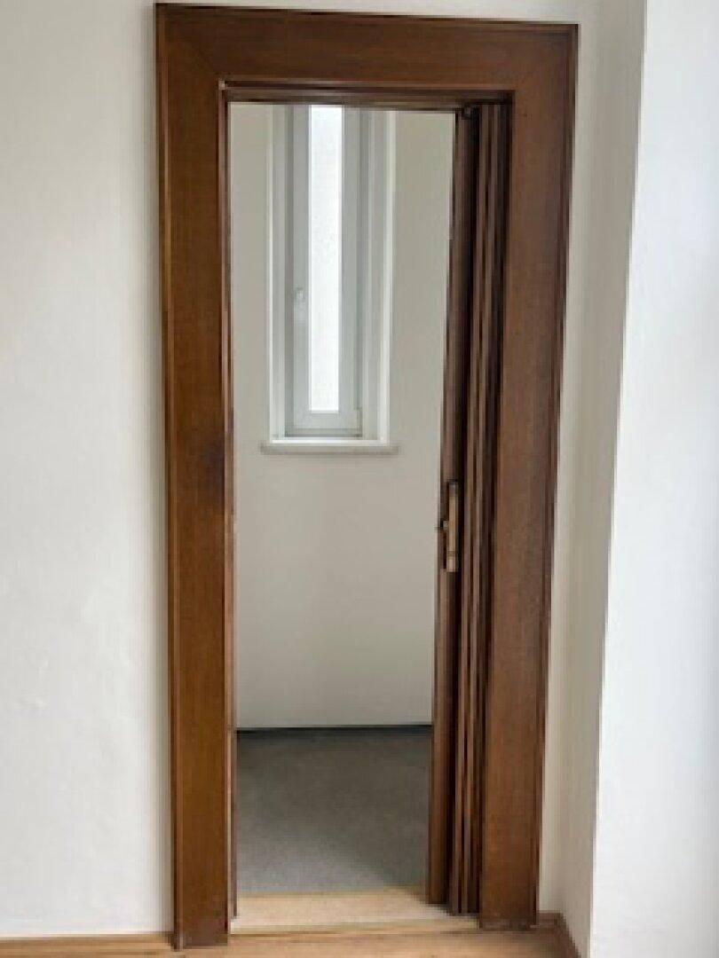 Holztürrahmen führt in einen hellen Raum mit Fenster.