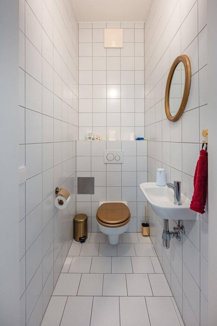 Kleines Gäste-WC mit weißen Fliesen, Toilette und Waschbecken.