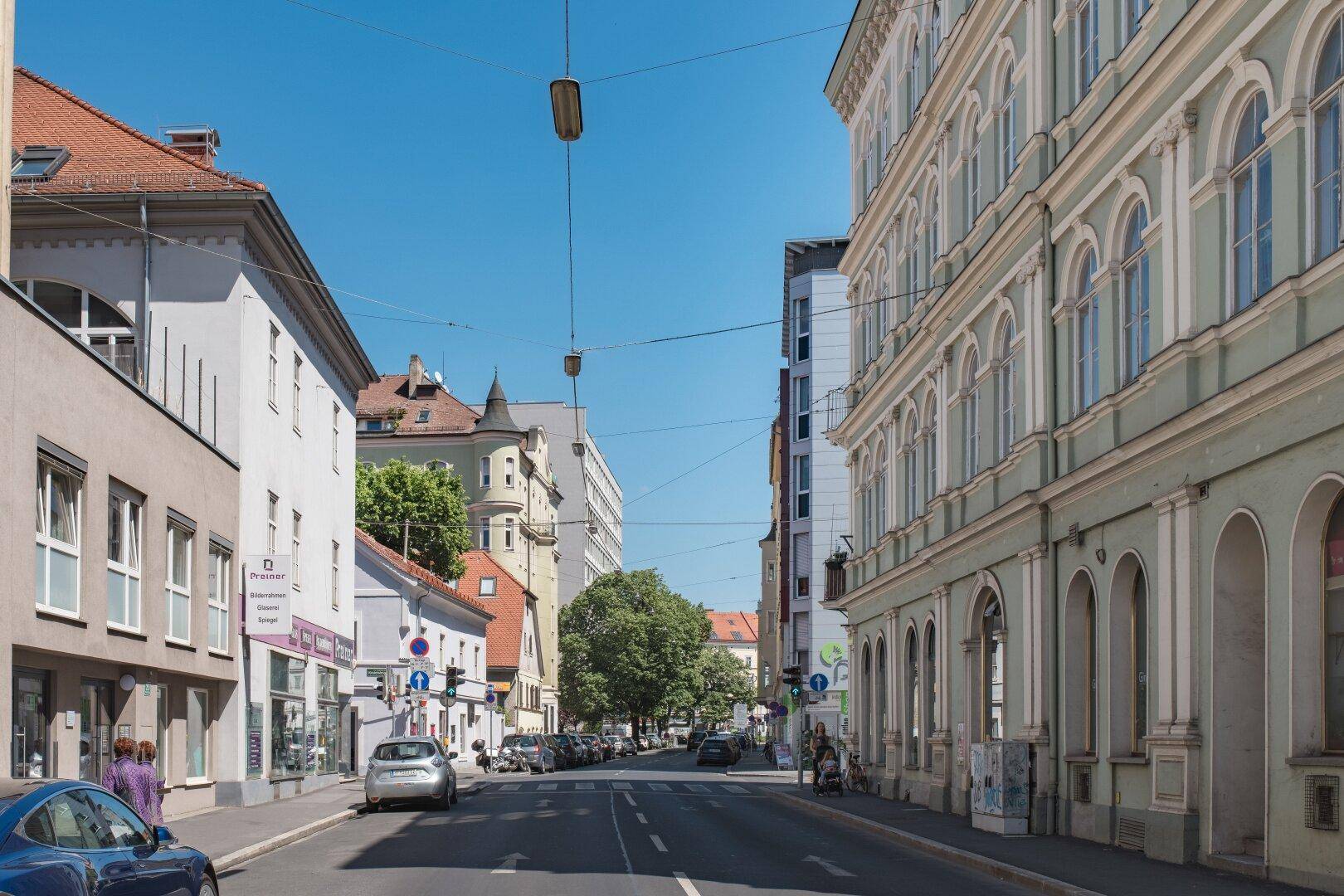 Belebtes Stadtbild mit historischen Gebäuden, Geschäften und geparkten Autos.