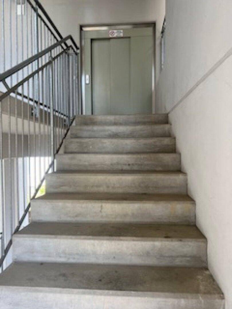 Treppenhaus mit Betontreppen und einem Aufzug, der die Etagen verbindet.
