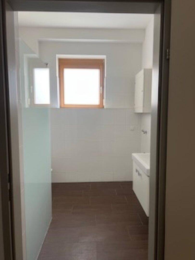 Helles Badezimmer mit Fenster, weißen Fliesen und dunklem Fliesenboden.