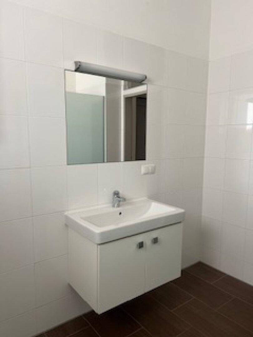 Modernes Badezimmer mit weißem Waschbecken, Spiegel und hellen Fliesen an den Wänden.